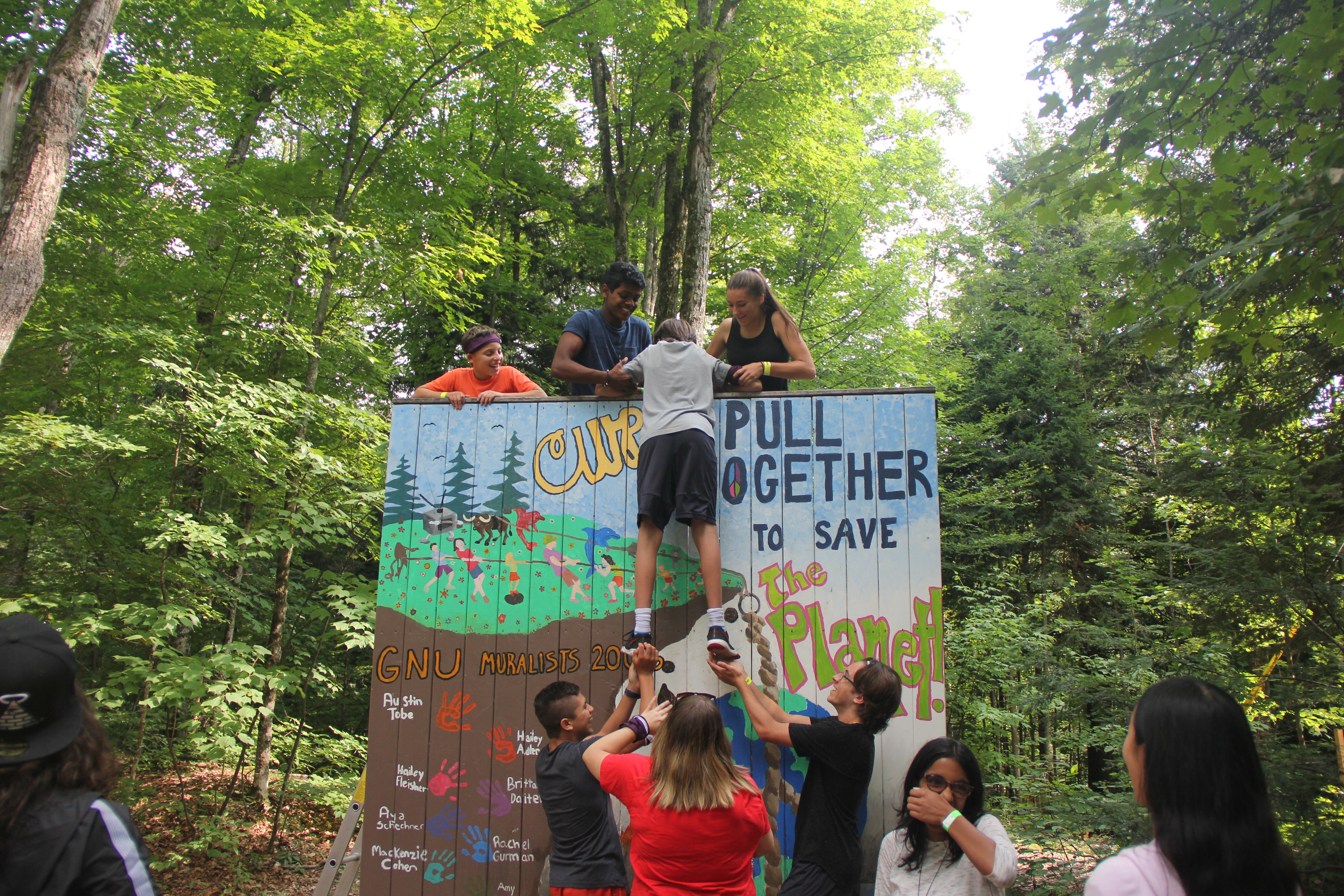 Youth having fun at camp doing a team building activity of pulling up each person over a wall